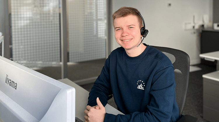 Auszubildender sitzt mit Headset am Ohr am Arbeitsplatz im Büro
